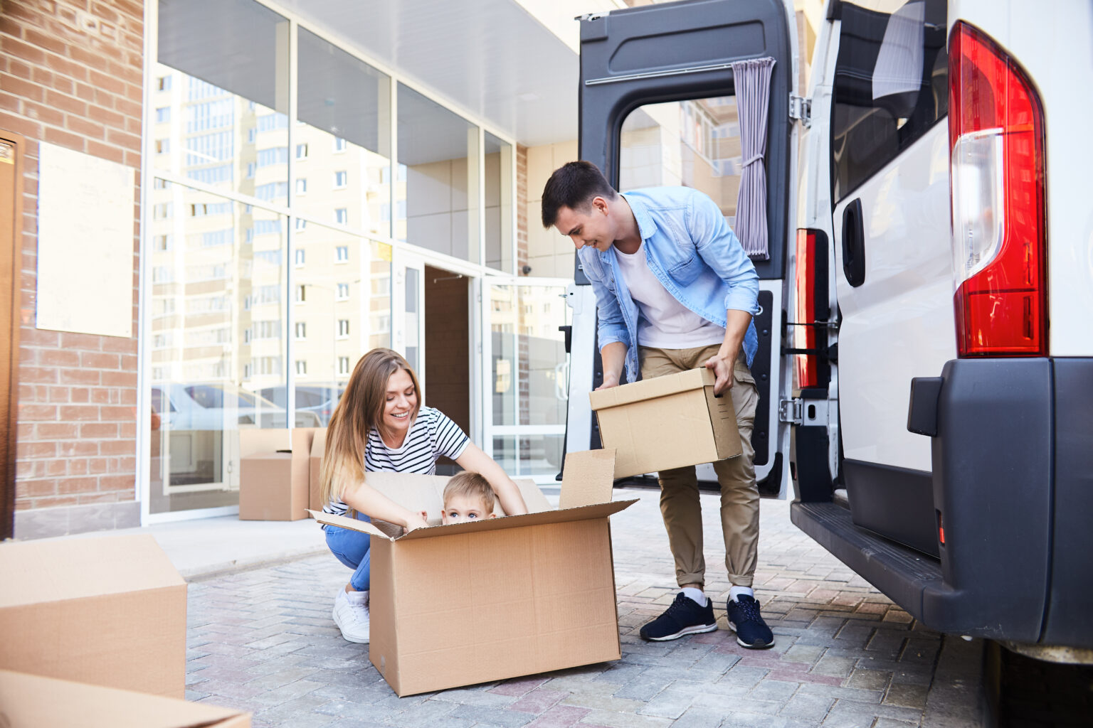 Portrait of happy young family with little child loading cardboard boxes into moving van outdoors